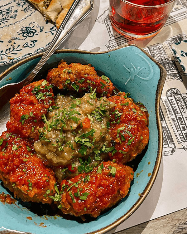 Dish with eggplant sauce surrounded by meat patties with tomato sauce and herbs.