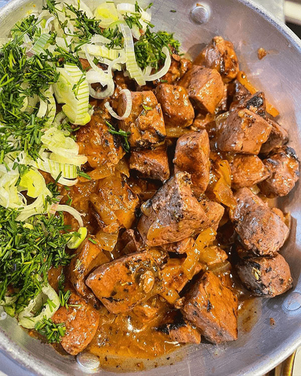 Meat-based dish with sauce, and chopped leak with herbs on the side.