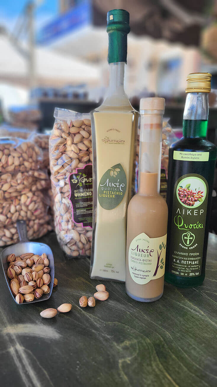 Product shot of a selection of pistachio liqueurs and pistachios in pachages and spread out on the countertop.