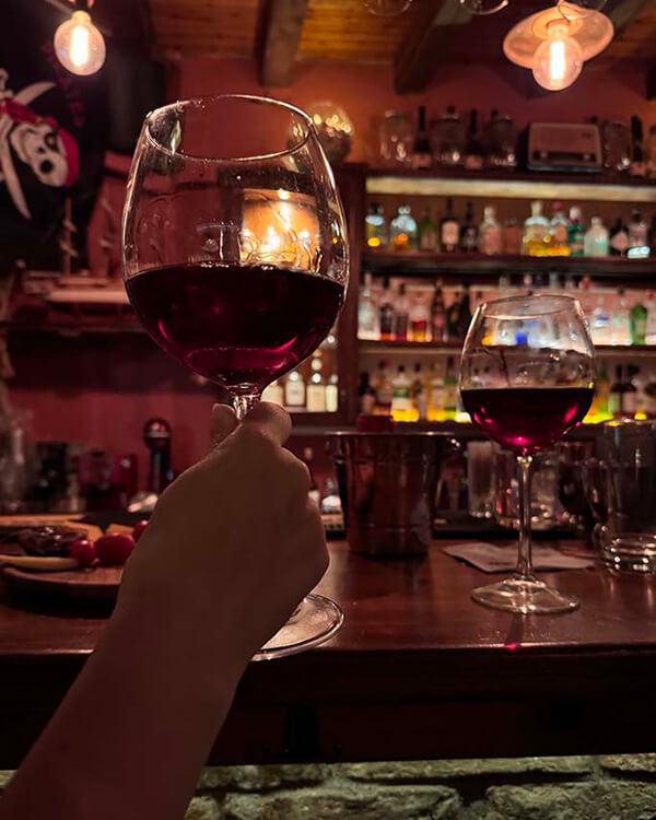 A hand holding a glass of red wine in front of the bar.